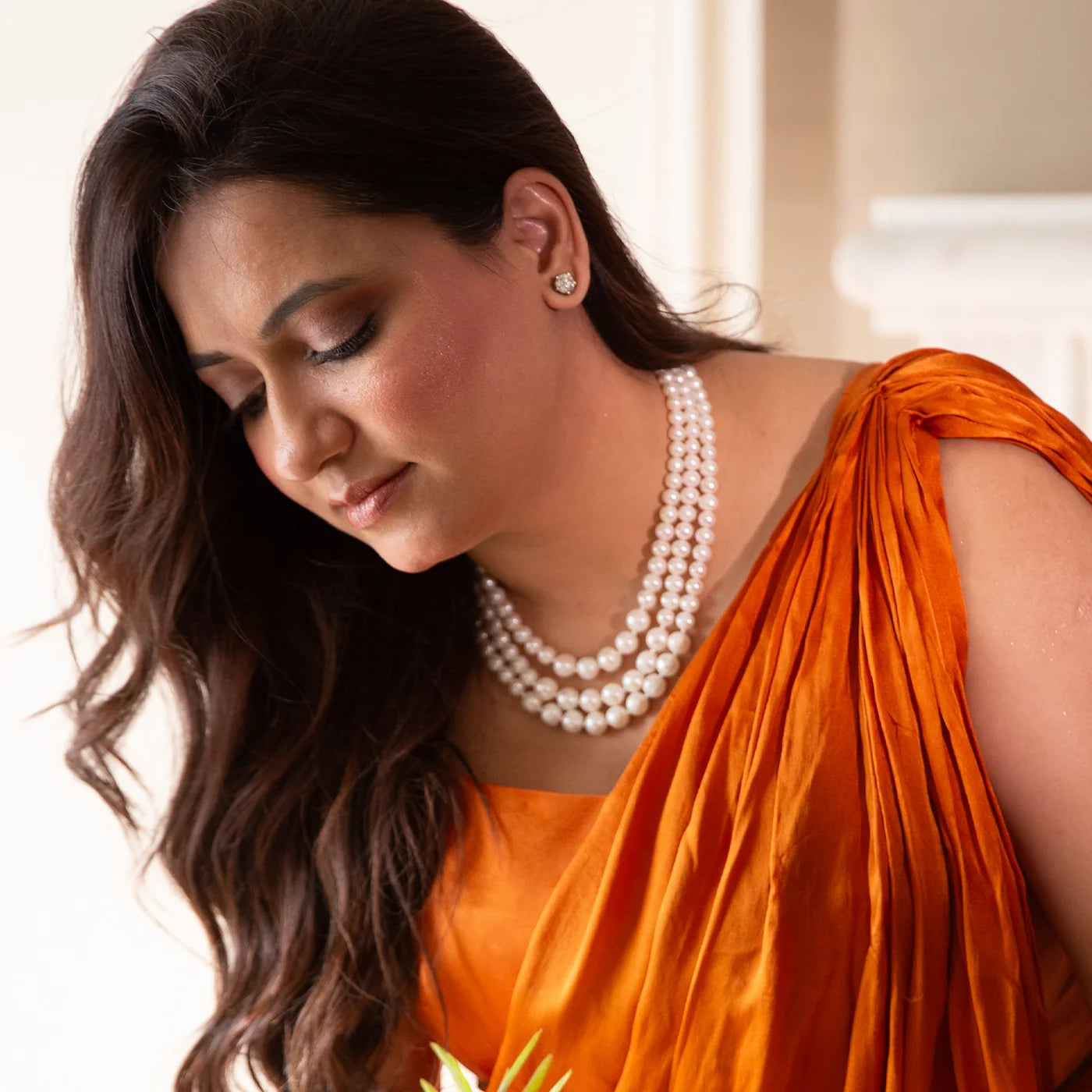 Woman wearing an orange saree with a pearl necklace, indoors.